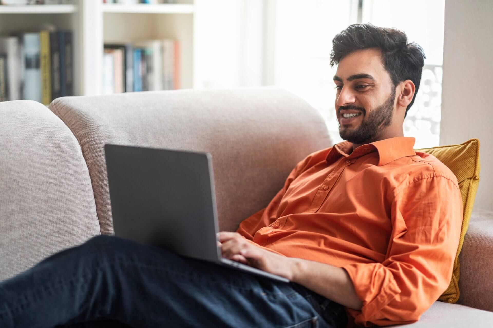 Hombre sonriente trabaja en el ordenador desde el sofá