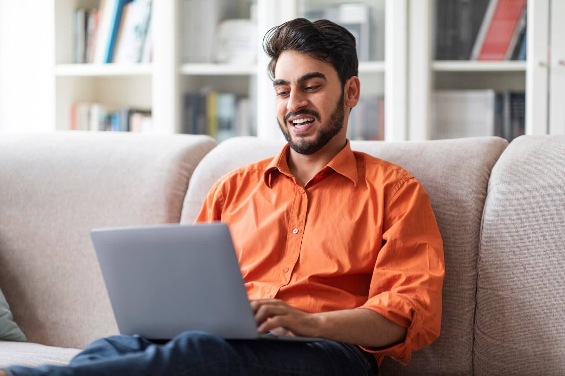 Hombre sonriente mientras trabaja en el ordenador desde el sofá