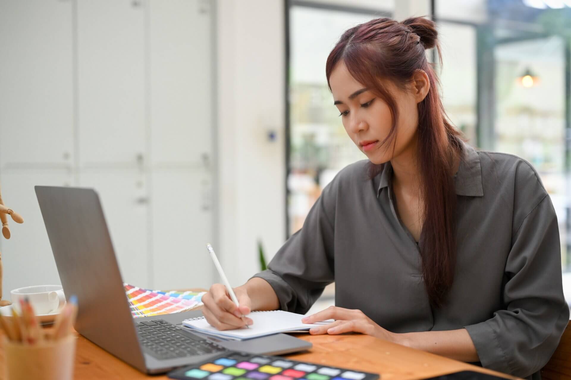 Mujer escribe libreta mientras trabaja ordenador