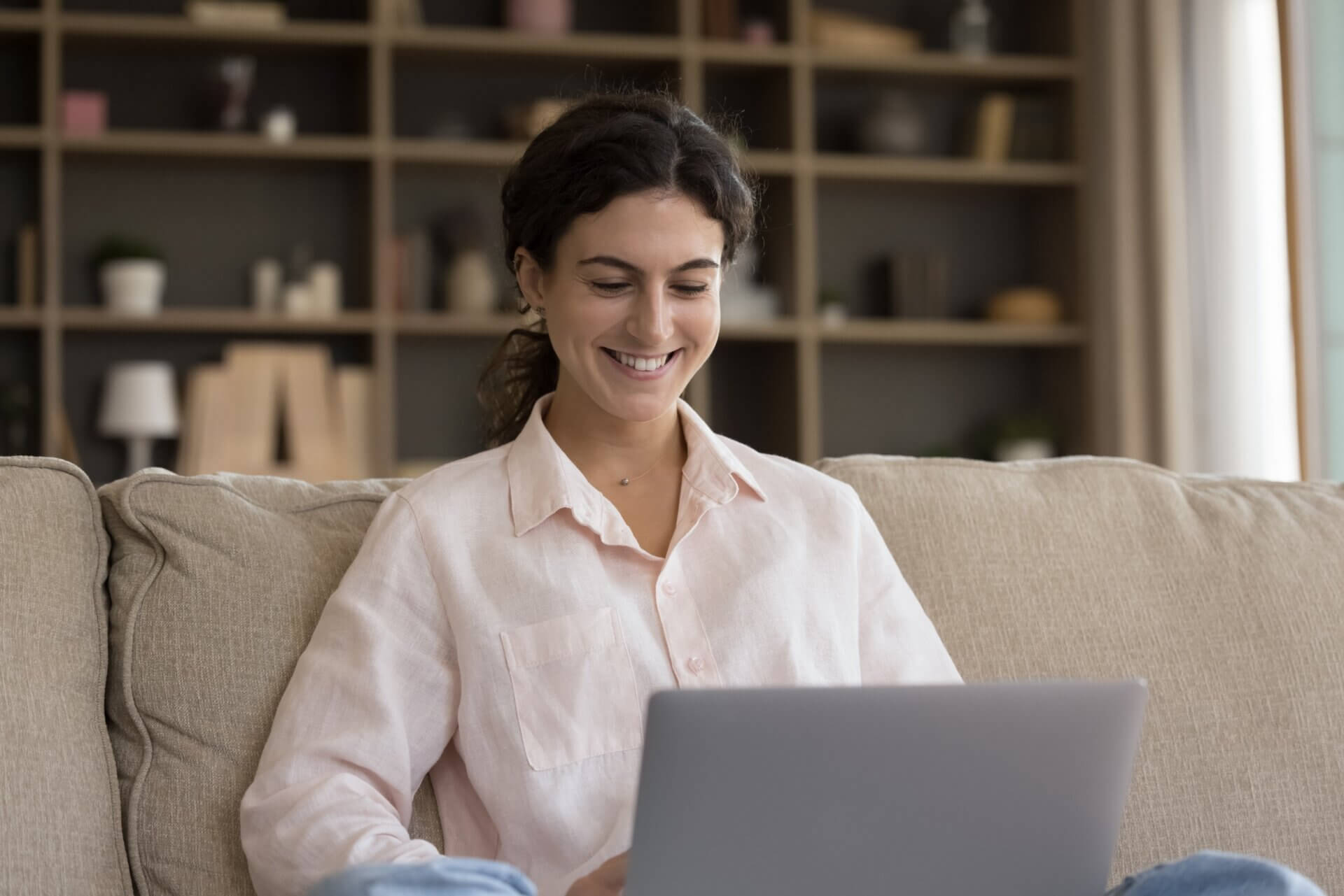 Mujer sonríe mientras trabaja en el ordenador desde el sofá