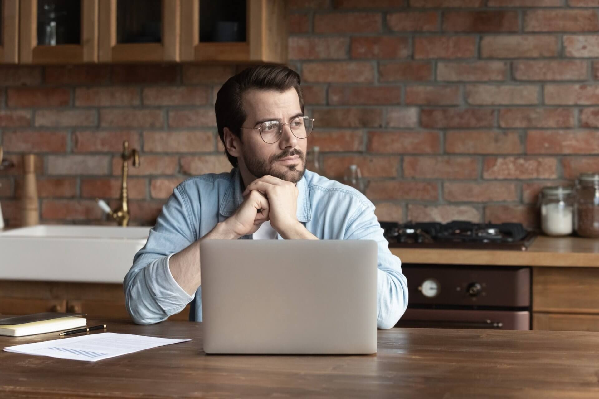 Hombre con gafas mira pensativo mientras trabaja en el ordenador