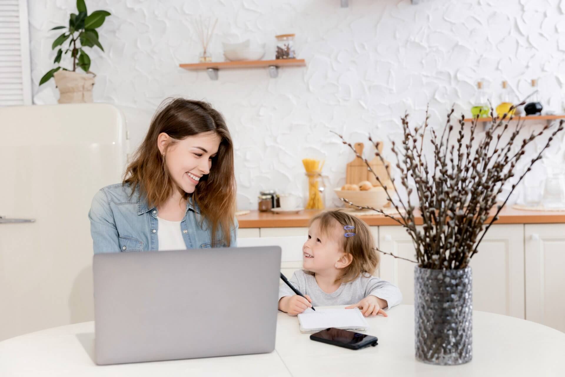 Mujer sonríe a su hija mientras trabaja en el ordenador