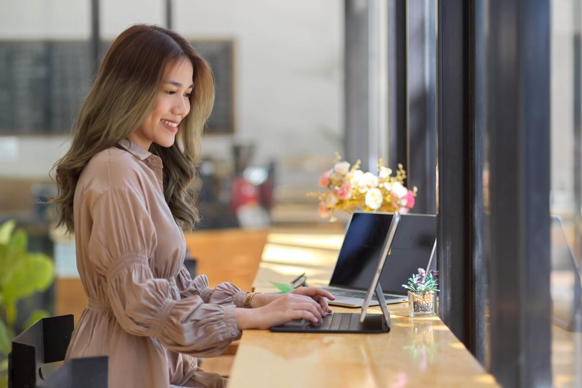Mujer sonriente trabaja en dos ordenadores desde un café