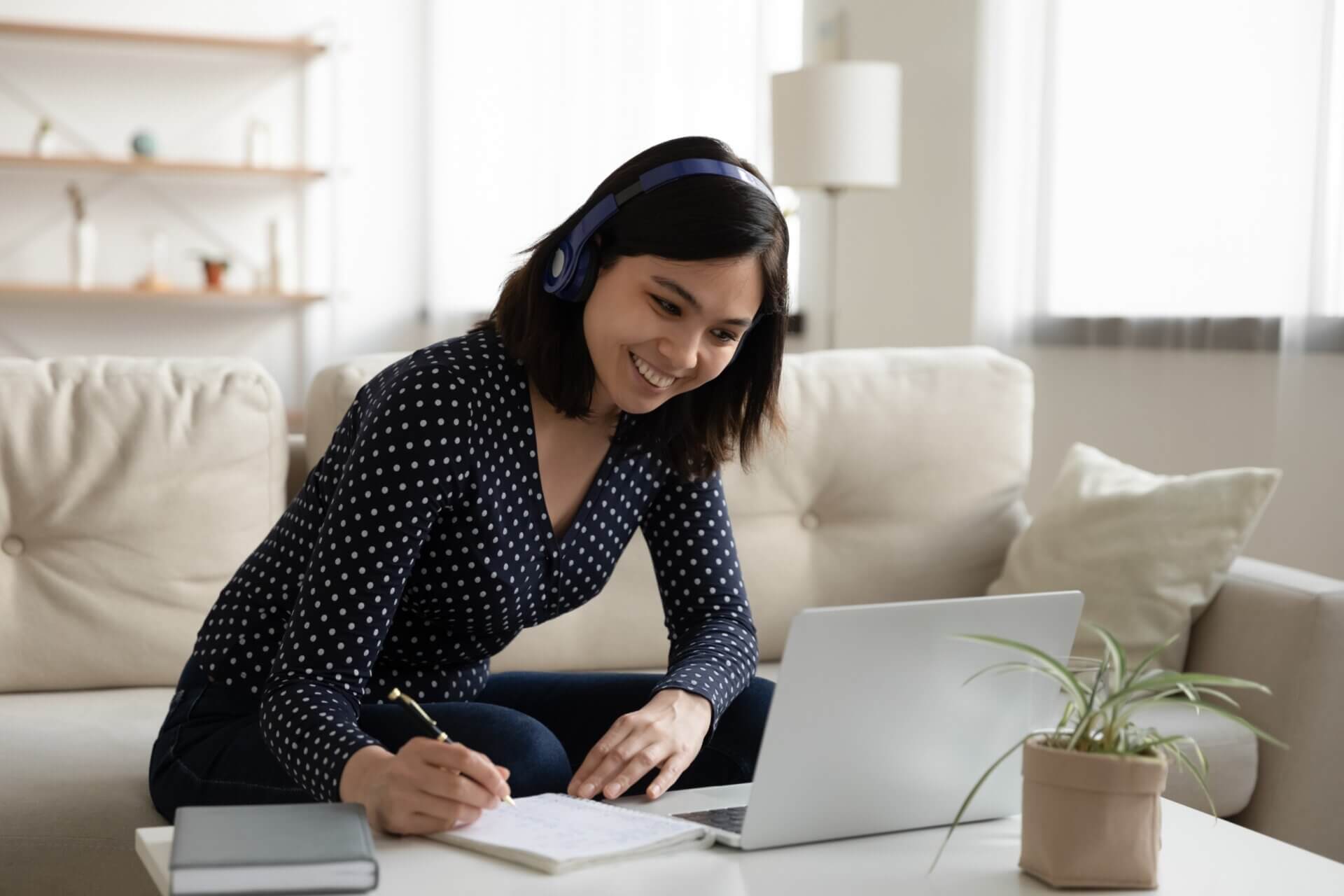 Mujer sonríe mientras trabaja en el ordenador y toma notas