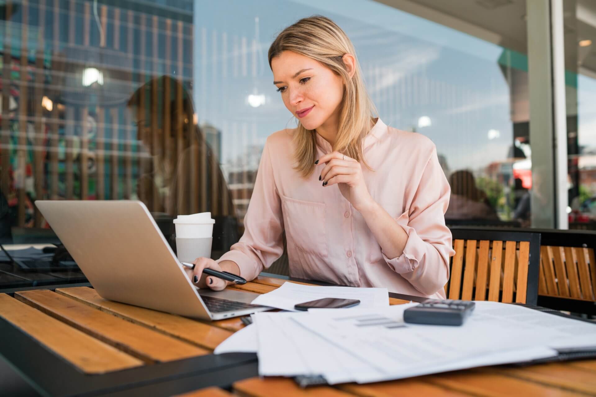 Mujer trabaja en un café con documentos y un ordenador