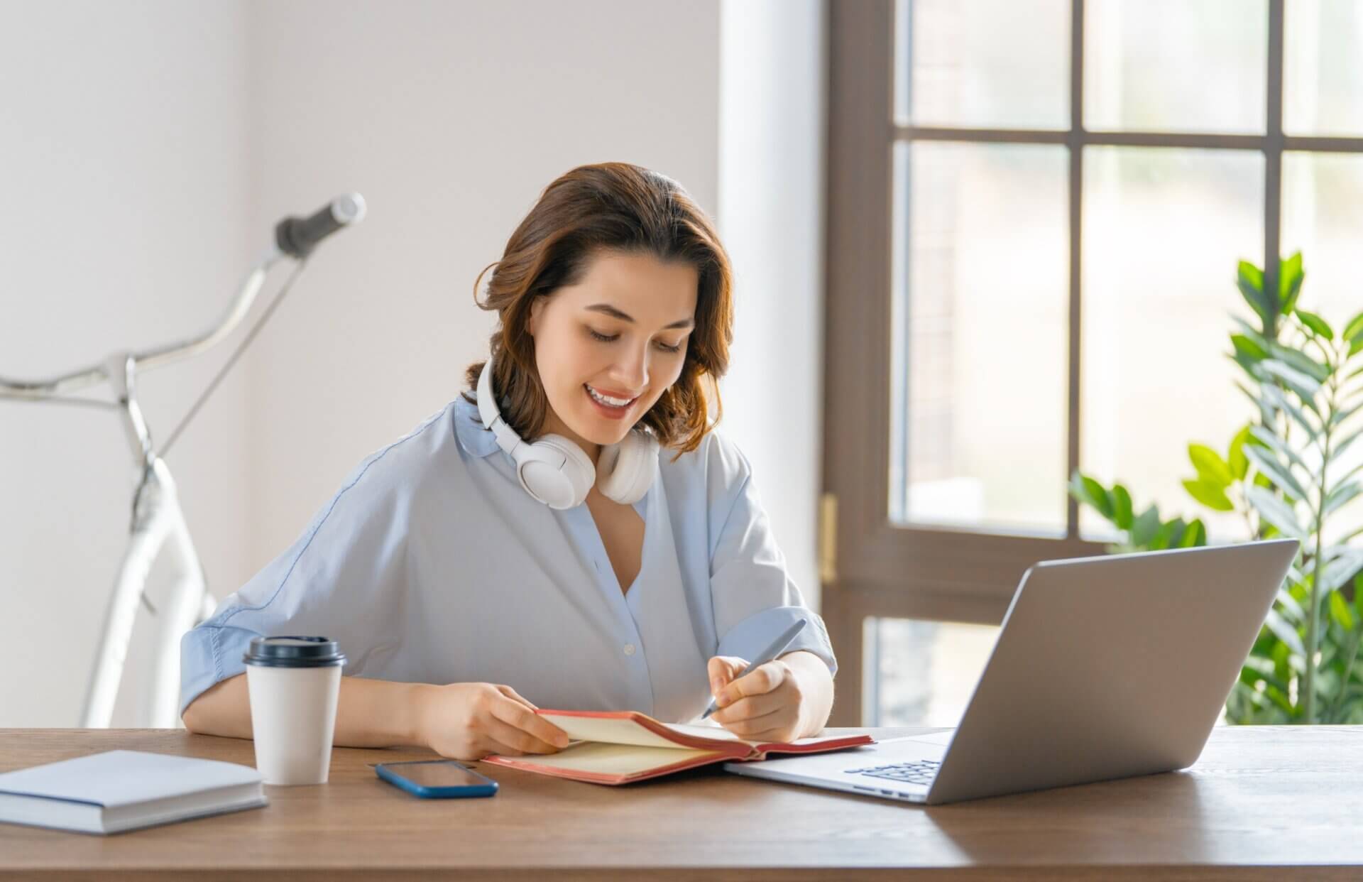 Mujer toma notas con los auriculares mientras trabaja en el ordenador