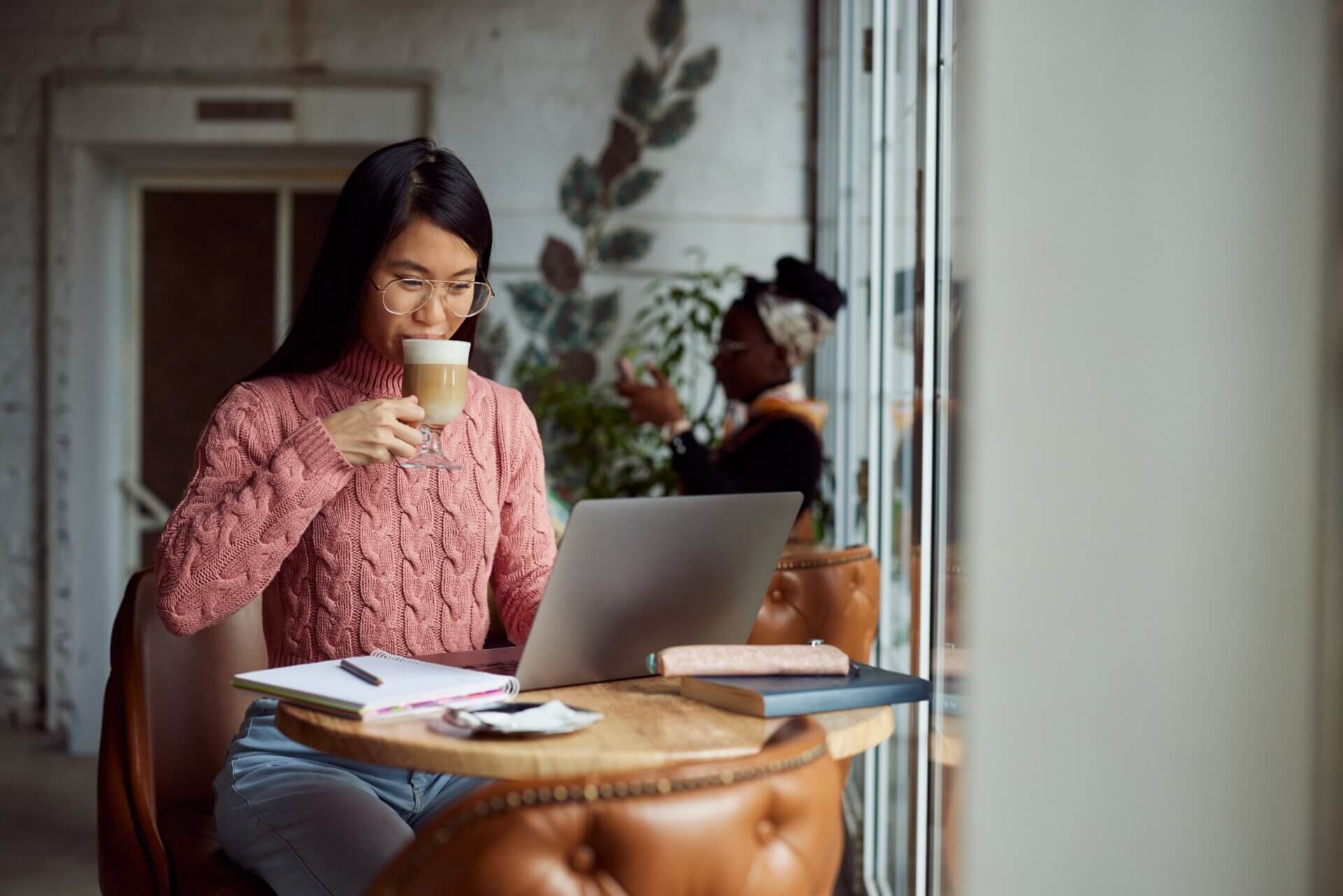 Mujer con gafas bebe café mientras trabaja en el ordenador