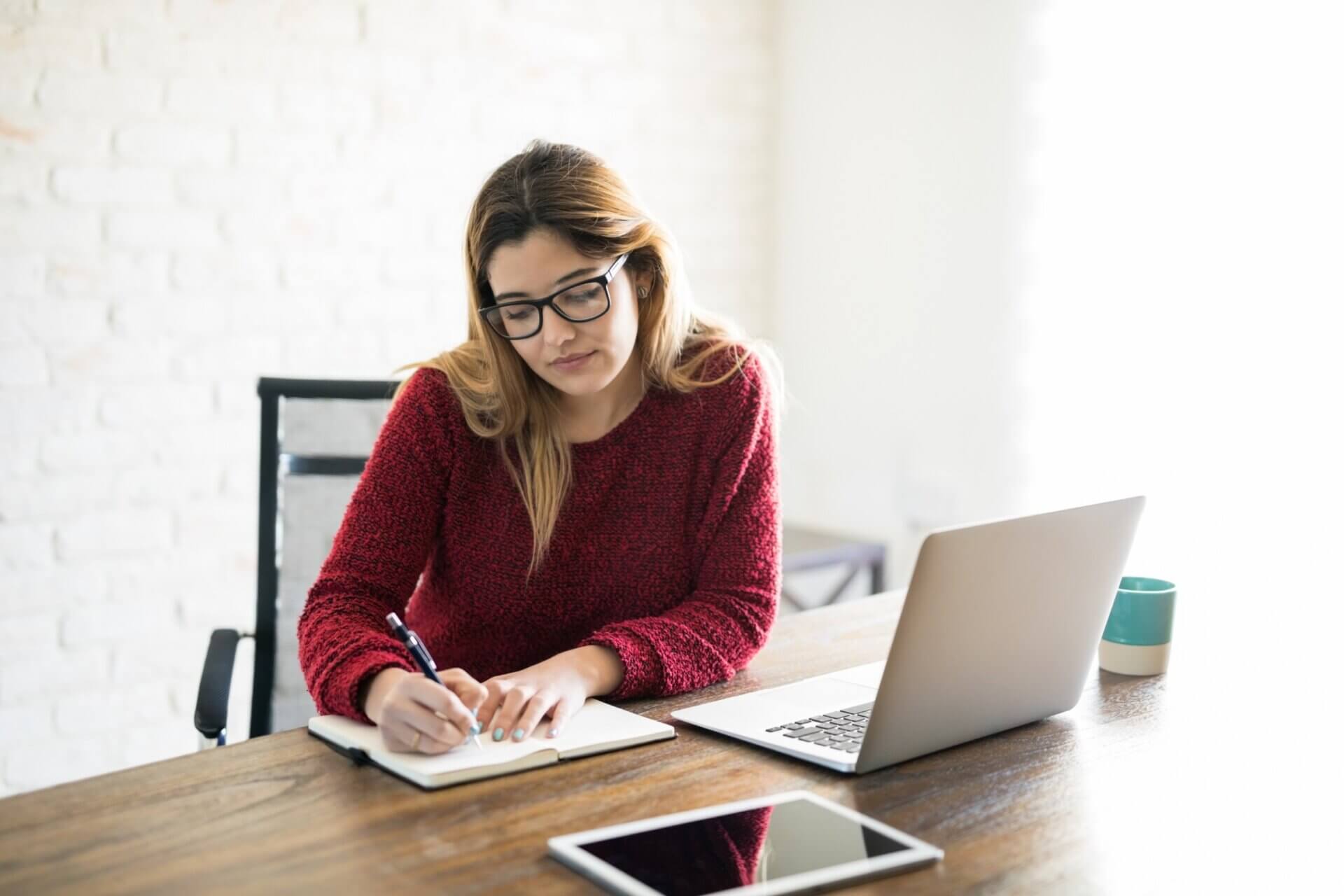 Mujer con gafas toma notas mientras trabaja en el ordenador