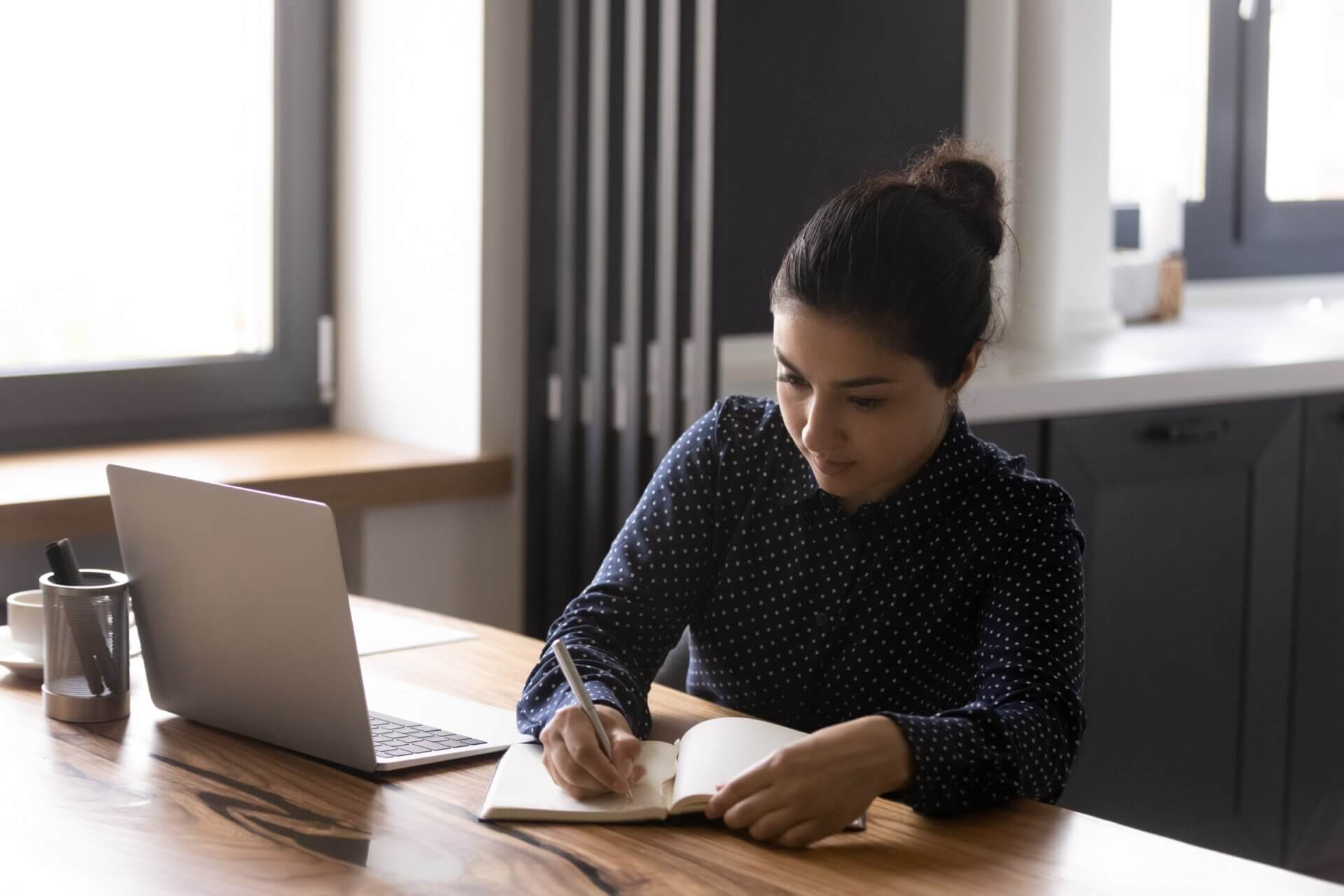Mujer escribe libreta mientras trabaja en el ordenador