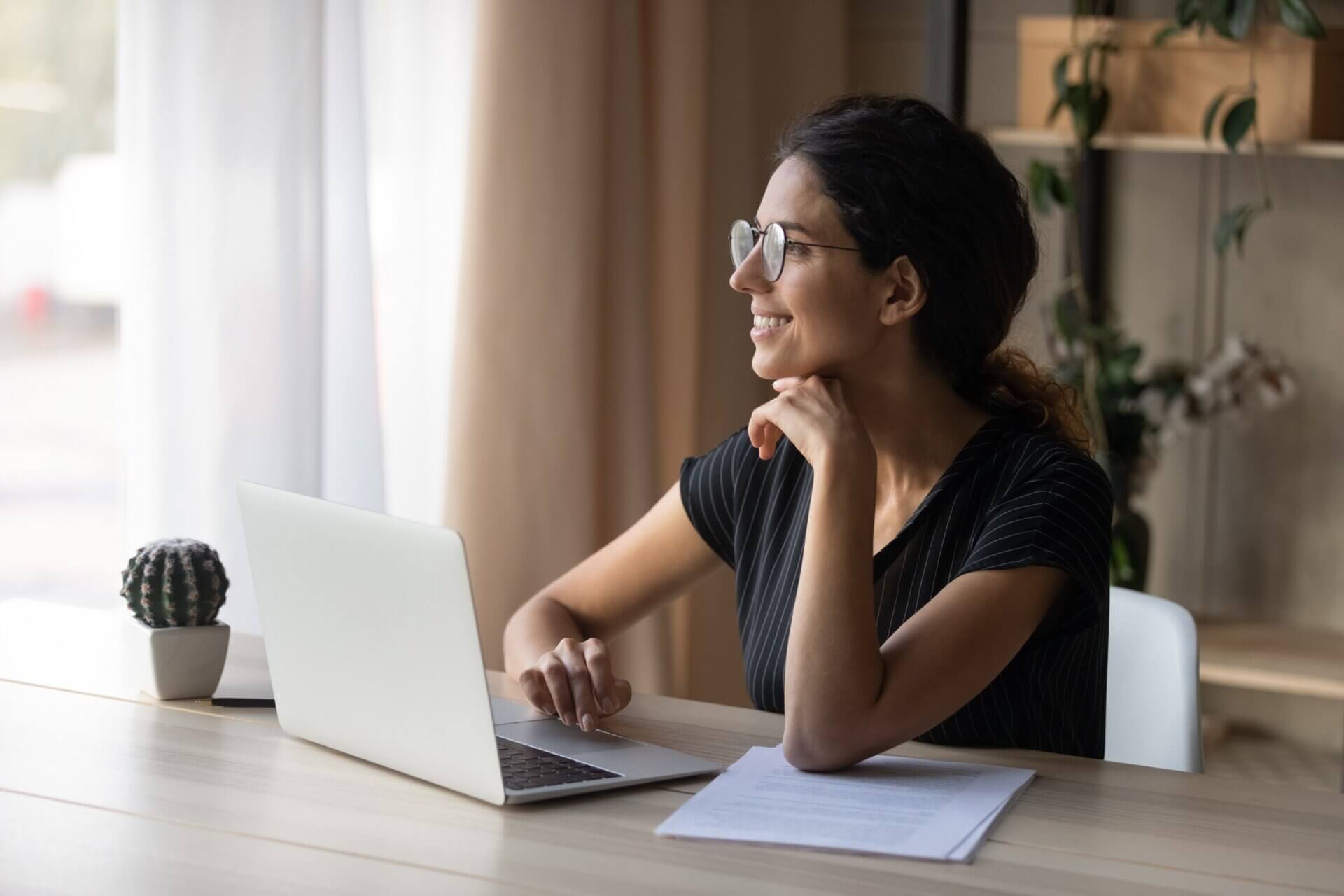Mujer sonríe mientras observa por la ventana frente al ordenador