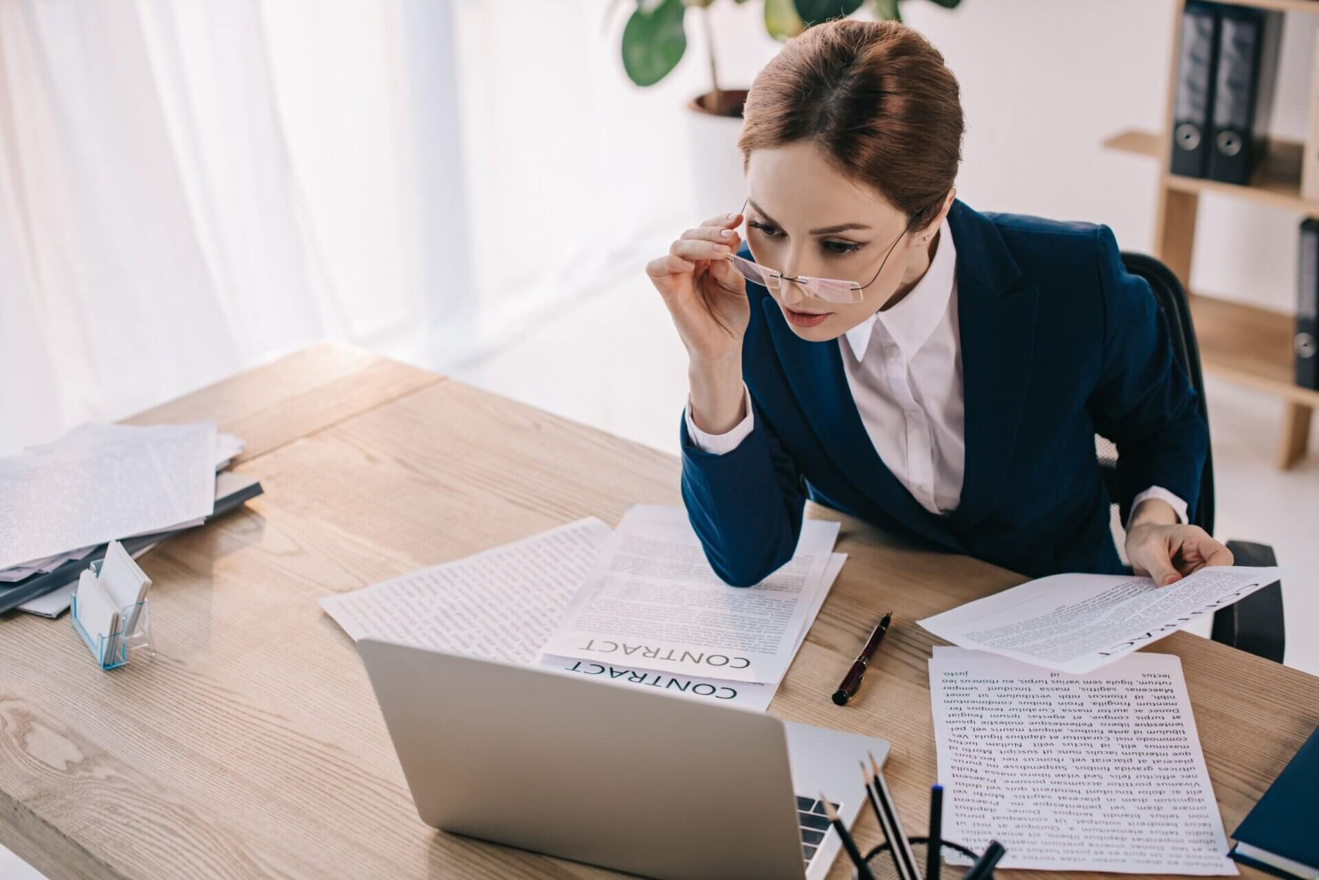 Mujer sostiene sus gafas con contratos sobre su escritorio