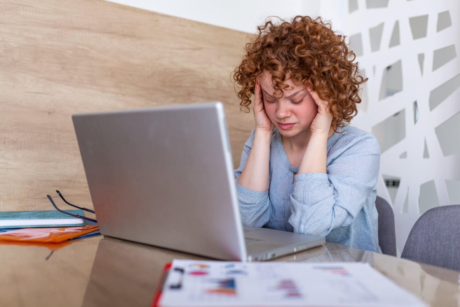 Mujer se sostiene la cabeza con frustración frente al ordenador